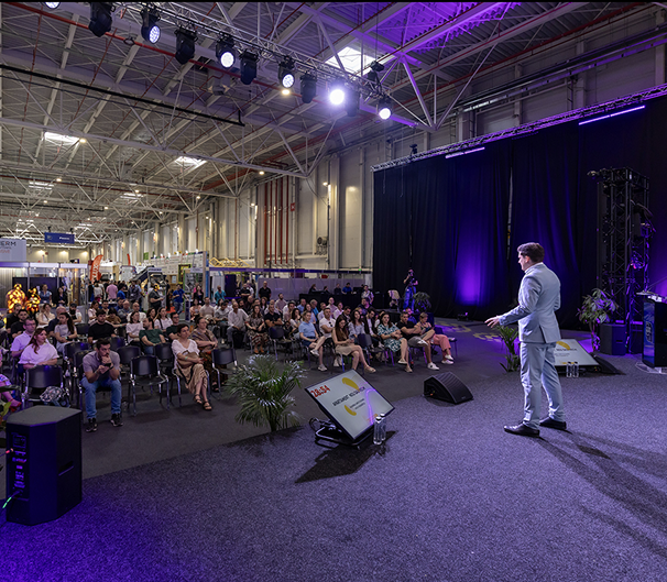 Speaker pe scenă la nZEB Expo cu iluminare violet și public în sală